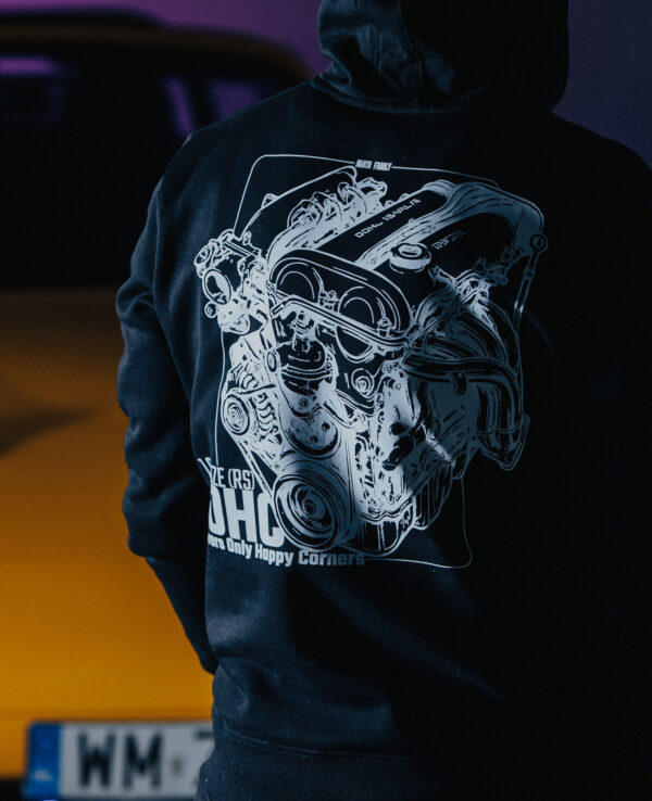 Person wearing a MiataFamily hoodie standing near a yellow sports car at dusk, showcasing car culture and community.