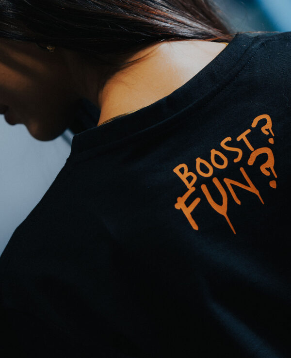 Close-up of a person wearing a black T-shirt with orange text that reads "Boost Fun?" on the back, highlighting casual automotive-inspired fashion.