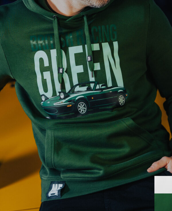 Close-up of a person wearing a green hoodie with a graphic of a Mazda Miata and the text "Building Green," emphasizing eco-friendly car culture.