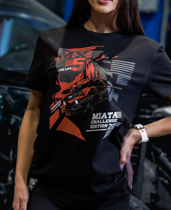 Woman wearing a Miata Challenge Edition 2023 T-shirt at a car event, showcasing Mazda Miata racing graphics and bold design elements.