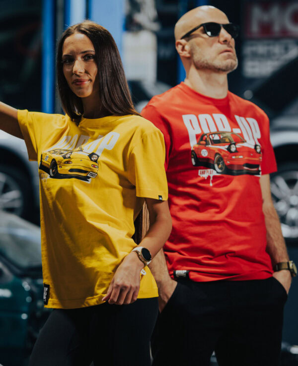 Two models wearing Miata-themed T-shirts at an auto show, showcasing Mazda Miata designs in yellow and red, highlighting car culture and Mazda enthusiasts.