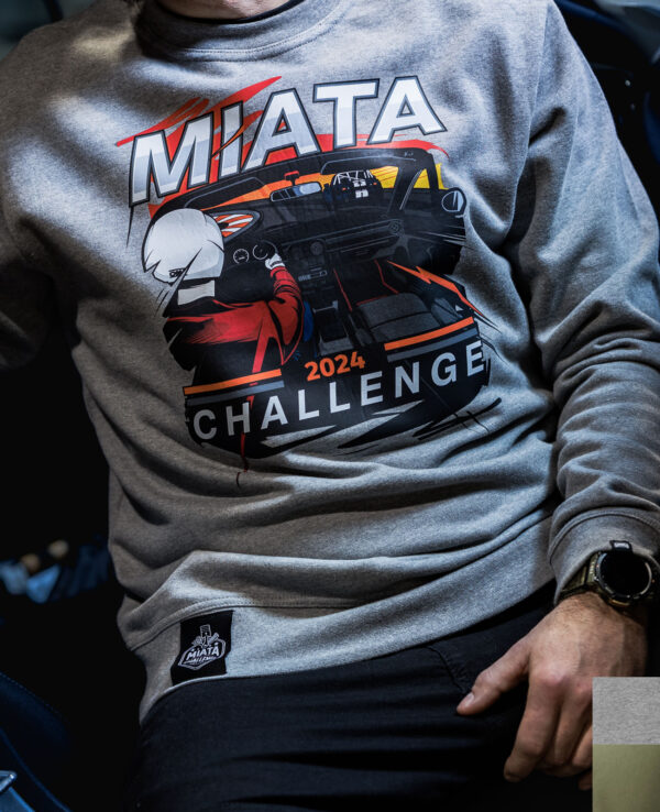 Close-up of a person wearing a gray Miata Challenge 2024 T-shirt featuring a graphic of a Miata car and racing elements.