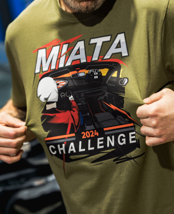 Close-up of a person wearing a green T-shirt with a Miata 2024 Challenge graphic design, featuring a racing car and dynamic elements.